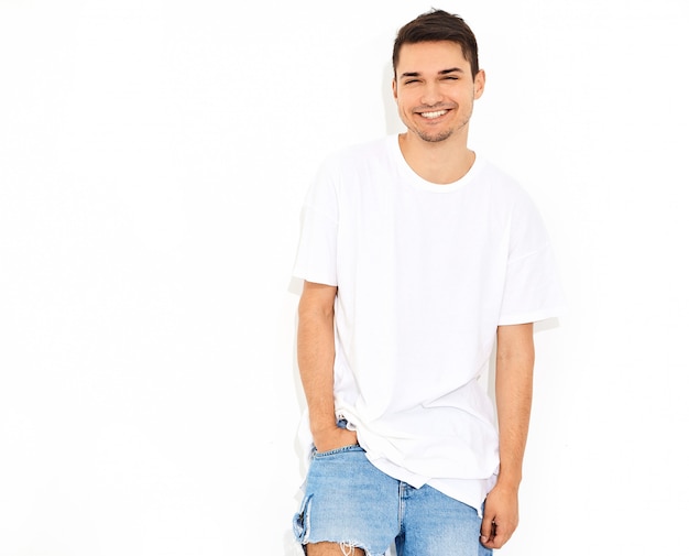 Foto grátis retrato de homem bonito modelo jovem sorridente, vestido com roupas jeans e posando de t-shirt. tocando sua cabeça