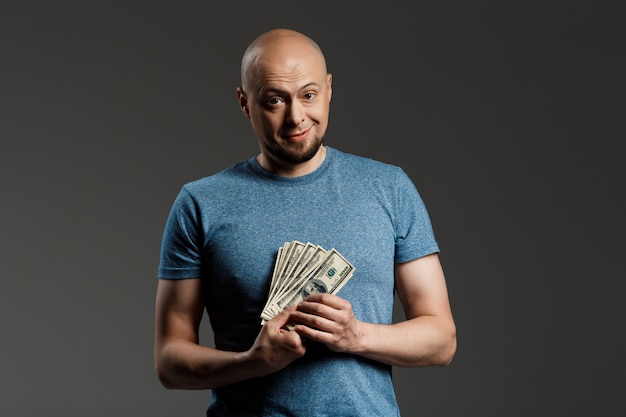 Retrato de homem bonito na camisa cinza, segurando o dinheiro sobre parede escura