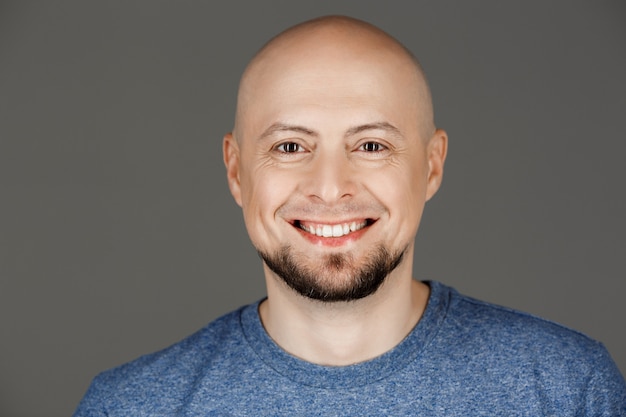 Foto grátis retrato de homem bonito na camisa cinza, sorrindo para a câmera sobre a parede escura