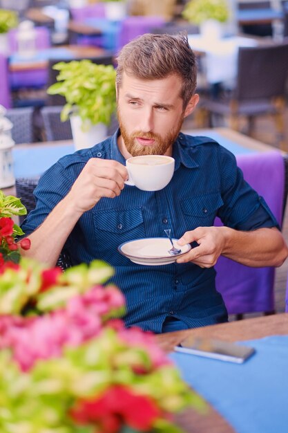 Retrato de homem casual ruiva barbudo bebe café em um café em uma rua.