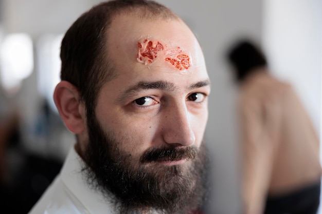 Retrato de homem com ferida sangrenta de zumbi, artista preparando maquiagem e efeitos especiais para transformar a pessoa em cadáver morto-vivo infectado. Projetando traje de terror assustador com rosto falecido.