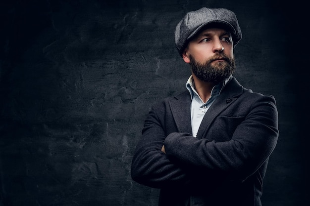 Retrato de homem de meia idade barbudo com braços cruzados no peito, vestido com um terno de lã e um gorro de tweed.