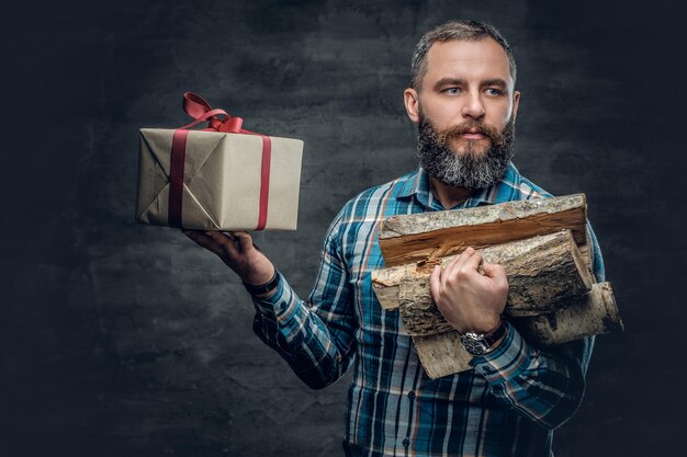 Retrato de homem de meia idade barbudo detém madeiras de fogo e caixa de presente de Natal.