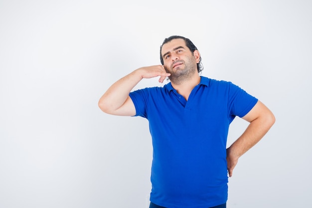 Foto grátis retrato de homem de meia-idade mostrando gesto de telefone em uma camiseta polo e olhando pensativo para a frente