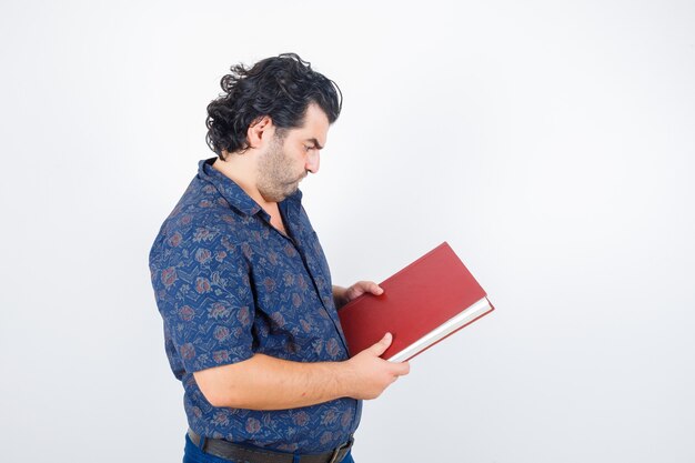 Retrato de homem de meia-idade olhando para um livro de camisa e olhando de frente com atenção