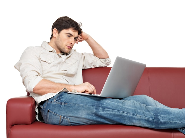 Retrato de homem descansando com laptop se senta no divã, isolado no branco.