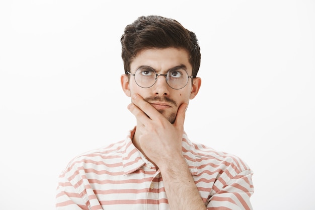 Retrato de homem determinado focado e criativo com bigode engraçado, esfregando o queixo, olhando para cima enquanto pensa, inventando uma ideia ou conceito, tentando resolver problemas matemáticos difíceis, fazendo cálculos