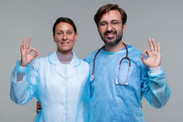 Retrato de homem e mulher vestindo aventais médicos e mostrando sinal de ok