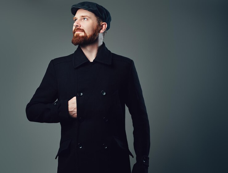 Foto grátis retrato de homem elegante de barba ruiva vestido com um boné liso de tweed e uma jaqueta preta sobre fundo cinza.