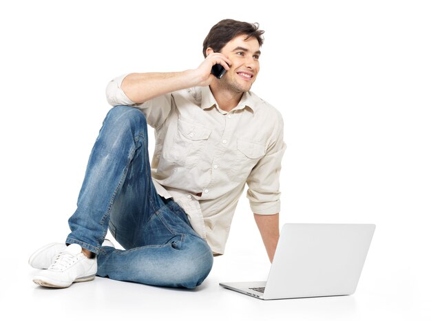 Retrato de homem feliz ligando pelo celular com o laptop em casuais isolado no branco.