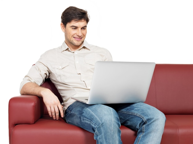 Retrato de homem feliz sorridente com laptop senta-se no divã, isolado no branco.