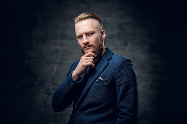 Retrato de homem hipster ruiva barbudo vestido com uma jaqueta azul sobre fundo cinza.