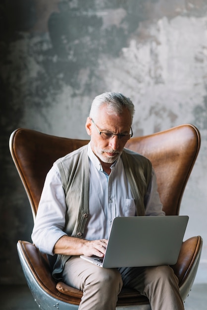 Retrato, de, homem idoso, sentar-se cadeira, usando computador portátil