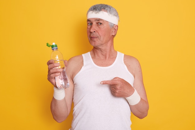 Retrato de homem idoso vestindo camiseta casual sem mangas e bandana, segurando a garrafa de água e apontando para ele com o dedo indicador