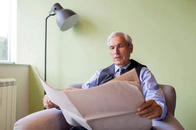 Retrato, de, homem negócios sênior, sentando, ligado, poltrona, jornal leitura