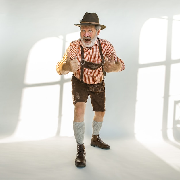 Retrato de homem sênior da Oktoberfest com chapéu, vestindo as roupas tradicionais da Baviera. Tiro completo masculino no estúdio em fundo branco. A celebração, feriados, conceito de festival. Gesto de bom.