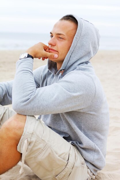 Retrato de homem sentado na praia e pensando