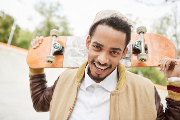 Retrato de jovem adolescente positivo praticando andar de skate ao ar livre, com expressão de felicidade