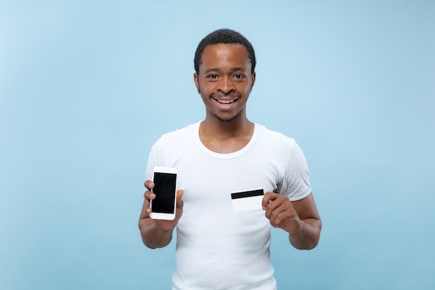 retrato de jovem afro-americano de camisa branca, segurando um cartão e um smartphone.