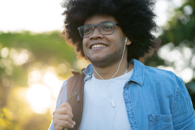 Retrato de jovem afro-latino ouvindo música com fones de ouvido enquanto caminha ao ar livre na rua