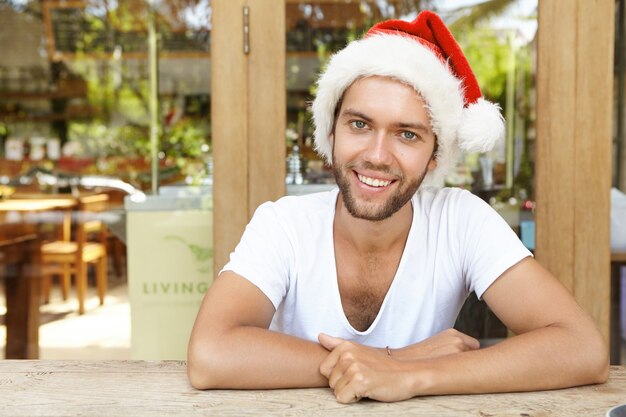 Retrato de jovem alegre e feliz com a barba por fazer vestida de chapéu vermelho com pelo branco se divertindo