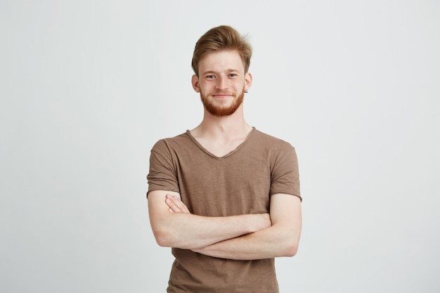 Retrato de jovem alegre feliz com barba sorrindo com braços cruzados.