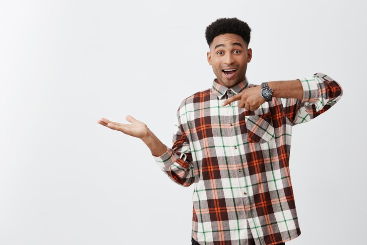 Foto grátis retrato de jovem alegre pele engraçada cara com penteado afro em camisa casual quadriculada fingindo segurando algo na palma da mão, apontando com a mão com expressão excitada