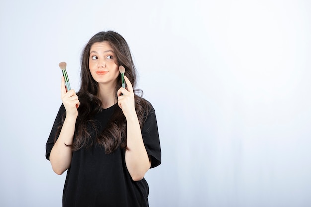 Retrato de jovem aplicando blush nas bochechas em fundo branco.