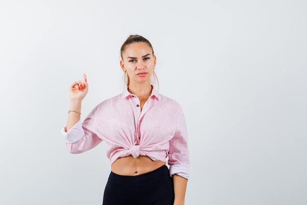 Retrato de jovem apontando para cima com camisa, calça e olhando de frente inteligente