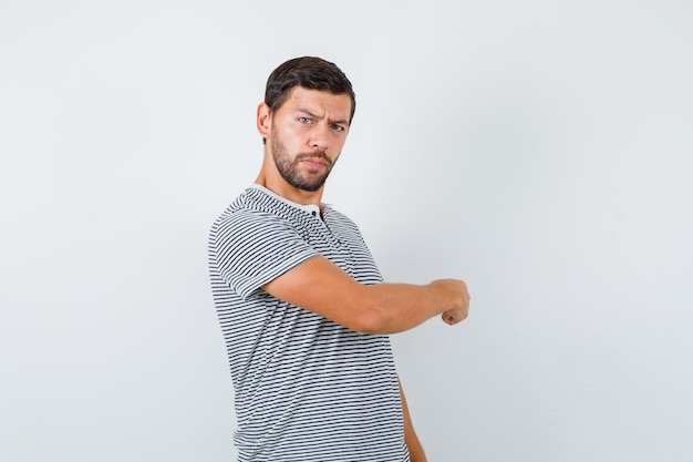 Retrato de jovem apontando para trás em uma camiseta e olhando hesitantemente vista frontal