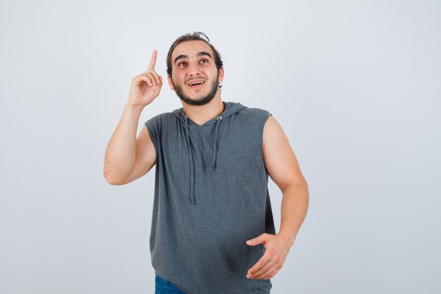 Retrato de jovem apto masculino apontando para cima enquanto cumprimenta o aperto de mão com um capuz sem mangas e uma vista frontal alegre