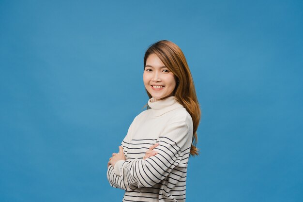 Retrato de jovem asiática com expressão positiva, braços cruzados, sorriso largo, vestida com roupas casuais e olhando para a frente sobre a parede azul