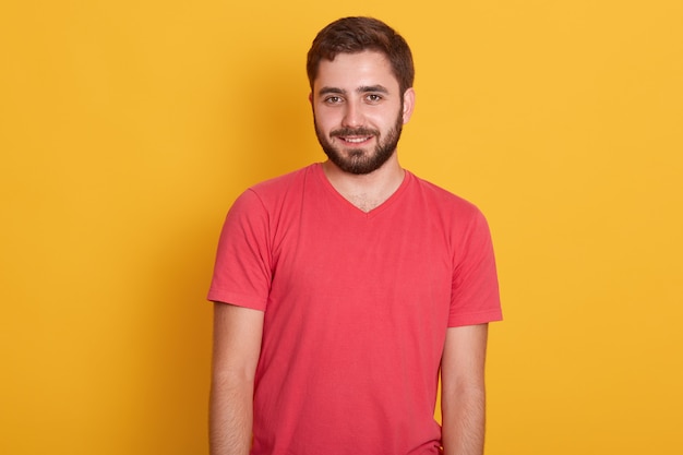 Retrato de jovem barbudo atraente feliz, bonito macho vestindo camiseta casual vermelha, sorrindo