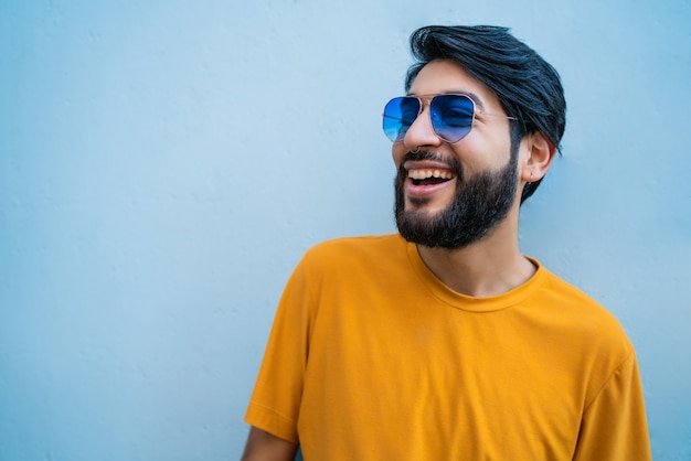 Retrato de jovem bonito com roupas de verão e óculos escuros contra o espaço azul.