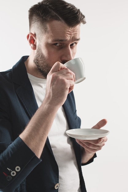 Retrato de jovem bonito elegante em pé no estúdio. homem vestindo jaqueta segurando uma xícara de café