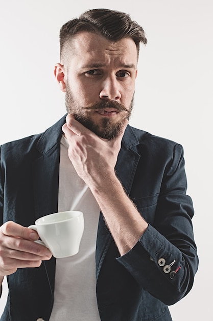 Retrato de jovem bonito elegante em pé no estúdio. homem vestindo jaqueta segurando uma xícara de café