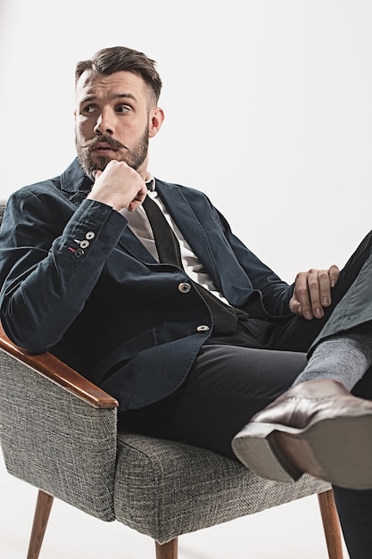 Retrato de jovem bonito elegante sentado contra branco. Homem vestindo jaqueta