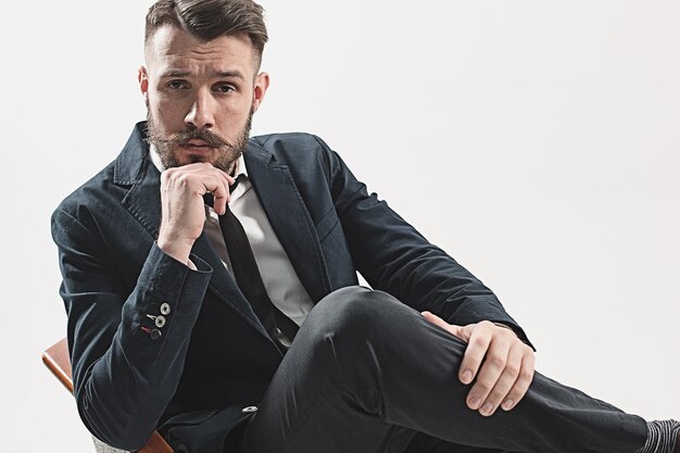 Retrato de jovem bonito elegante sentado no estúdio contra branco.