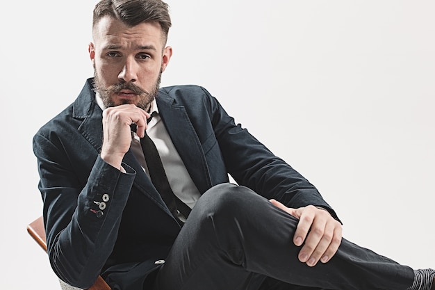 Retrato de jovem bonito elegante sentado no estúdio contra branco.