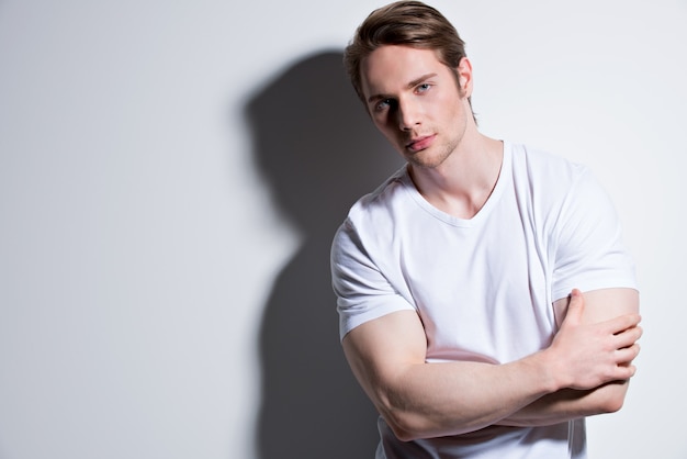 Foto grátis retrato de jovem bonito em poses de camiseta branca na parede com sombras de contraste.