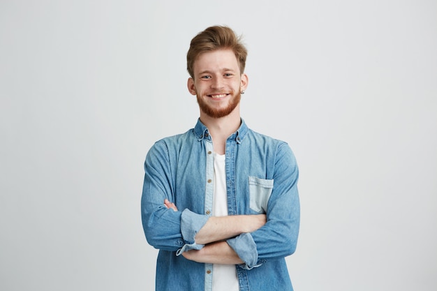 Retrato de jovem bonito na camisa jeans, sorrindo com braços cruzados.