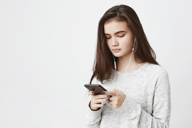 Retrato de jovem bonito, olhando concentrado na tela do telefone enquanto ouve música