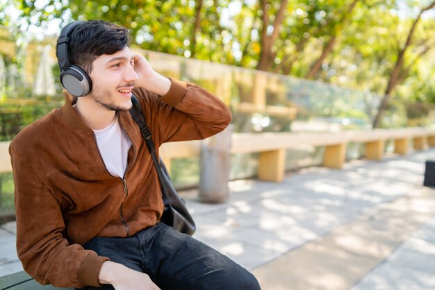 Retrato de jovem bonito ouvindo música com fones de ouvido enquanto está sentado ao ar livre. Conceito urbano.