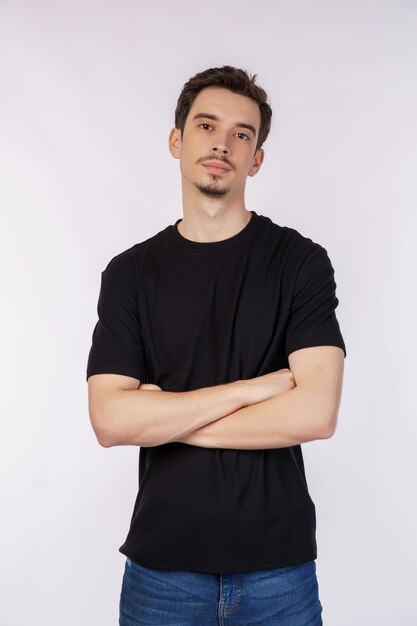 Retrato de jovem bonito vestindo camiseta preta em pé com braços cruzados com isolado no fundo branco do estúdio