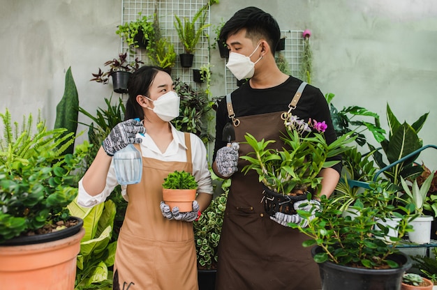 Retrato de jovem casal asiático de jardineiro vestindo avental, usando equipamento de jardim e ajudando a cuidar da planta de casa na loja