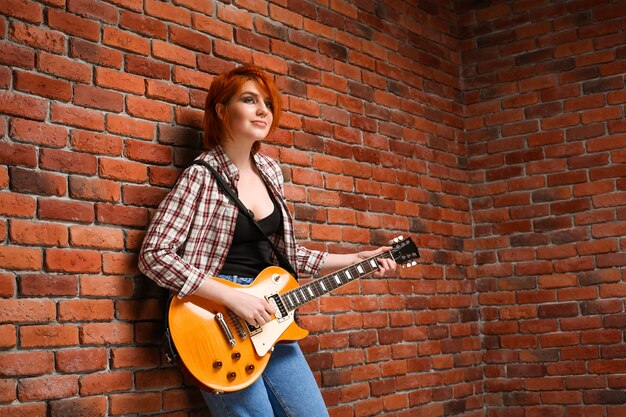 Retrato de jovem com guitarra sobre fundo de tijolo.