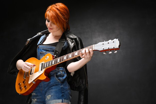 Retrato de jovem com guitarra sobre fundo preto.