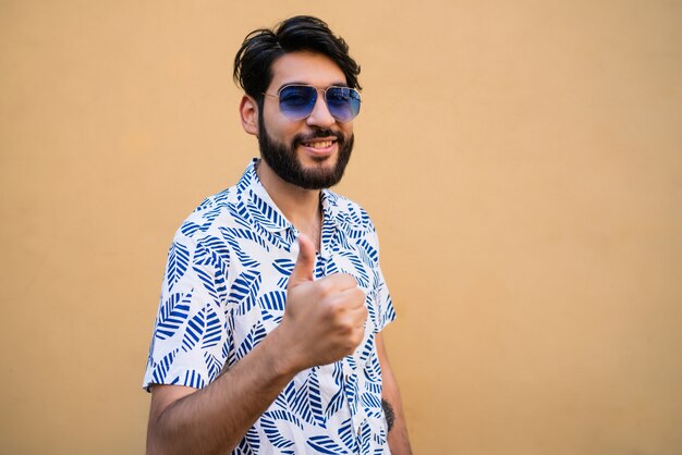 Retrato de jovem com roupas de verão e polegares contra o espaço amarelo.