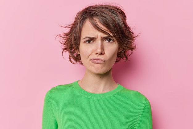 Retrato de jovem descontente carrancas rosto tem lábios de bolsas de expressão de mau humor tem penteado curto usa jumper verde isolado dover rosa studio fundo. conceito de emoções humanas negativas