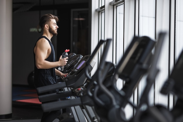 Retrato de jovem desportista fazendo exercícios aeróbicos e bebendo água no ginásio